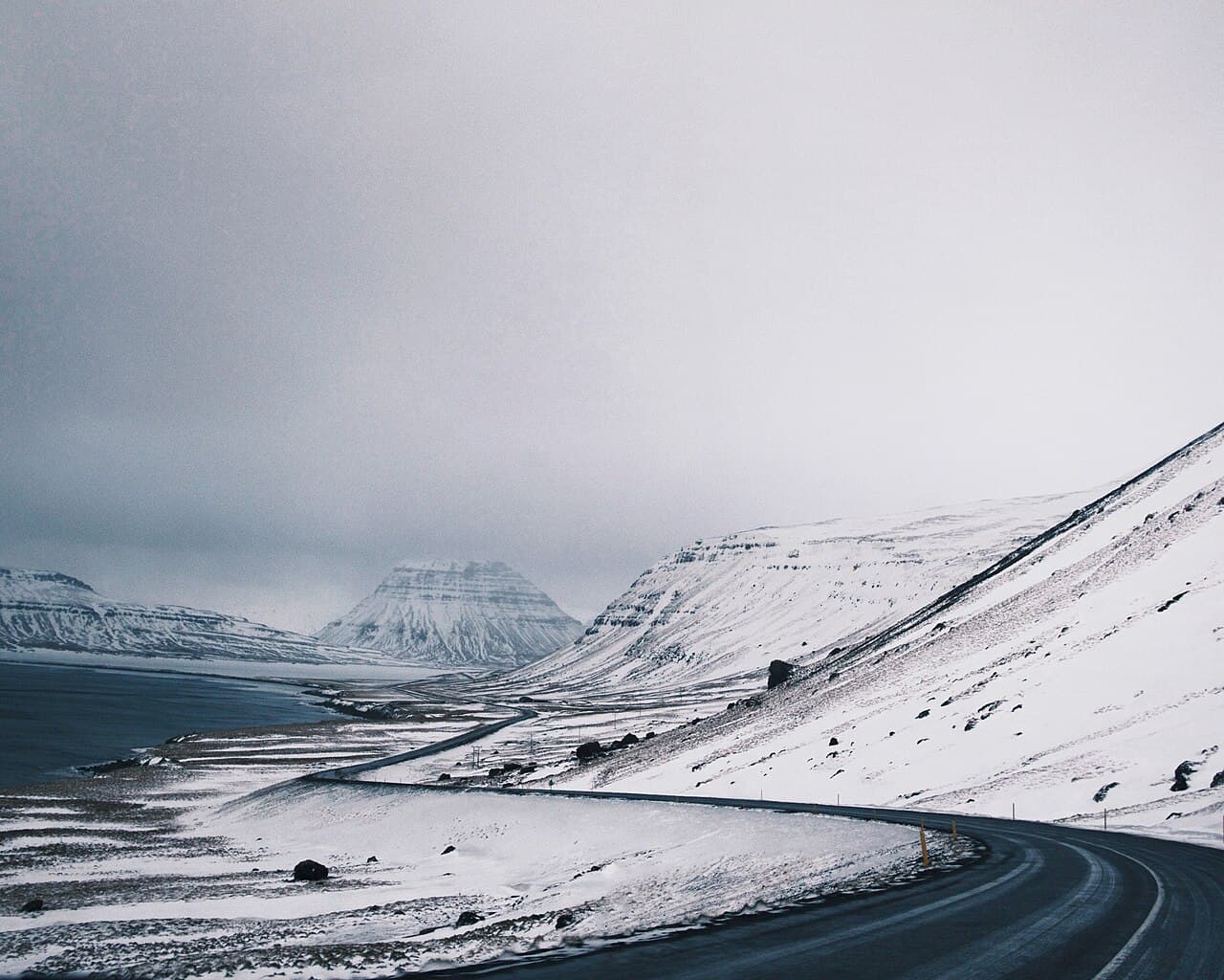 A snow-covered road across open country in Iceland in winter, under low light